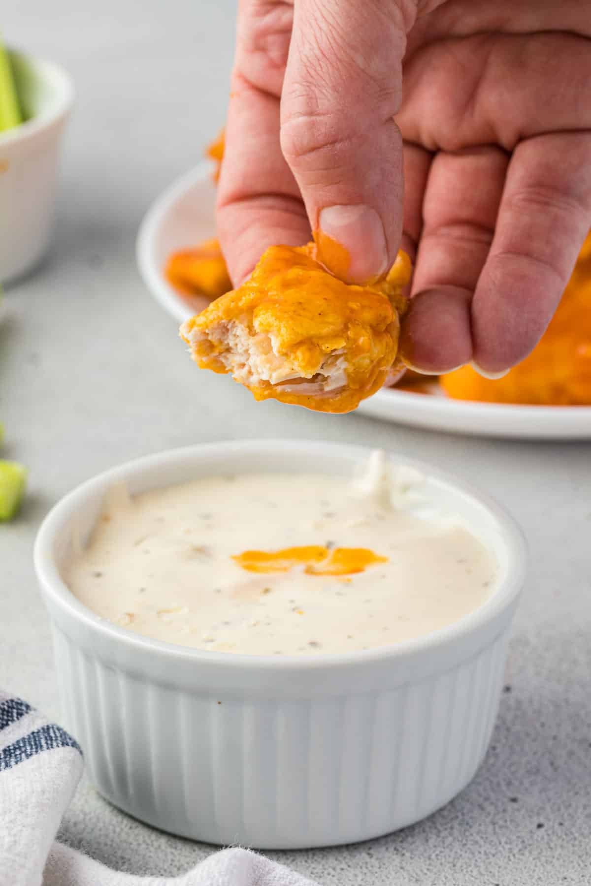 A hand holding a boneless wing with a bite out of it, over a bowl of ranch.