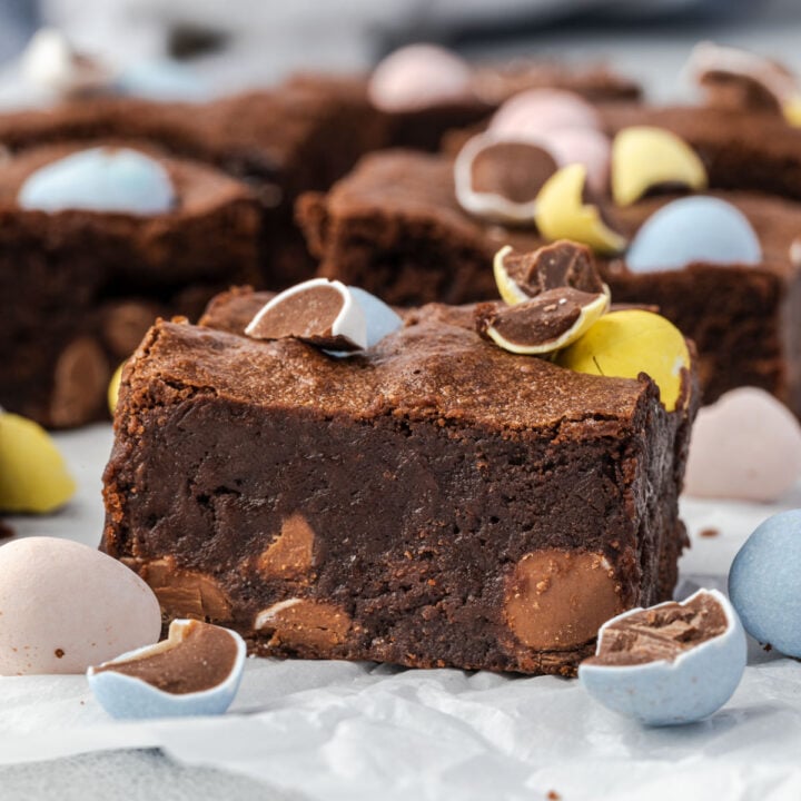 Side angle view of a rich and fudgy brownie square topped with chocolate egg candies and more brownies in background.