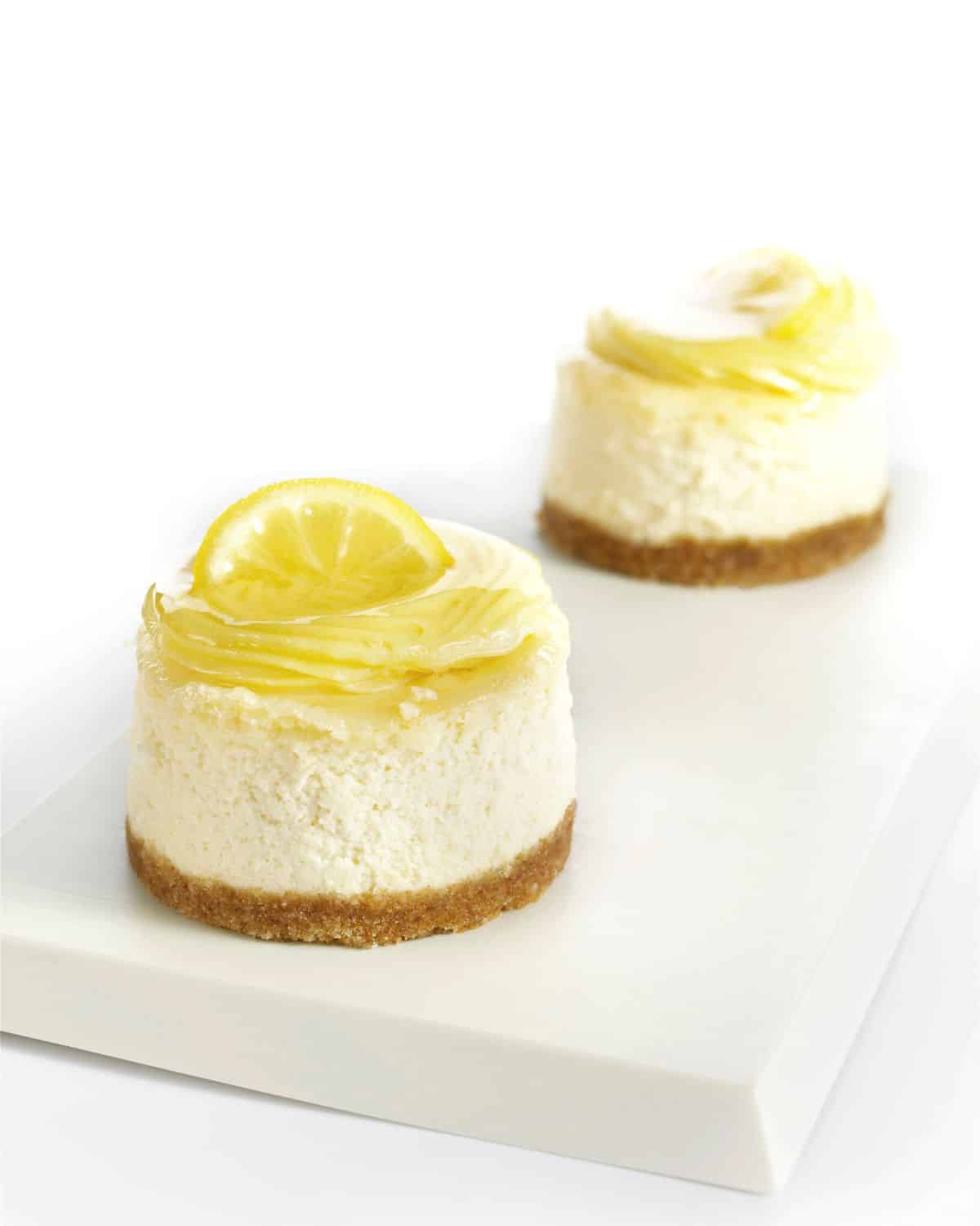 Two mini-no bake lemon cheesecakes on a rectangular board.