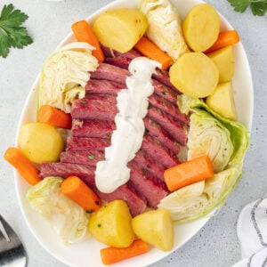 Ovel platter with corned beef and vegetables, and creamy mustard sauce drizzled down center of beef.