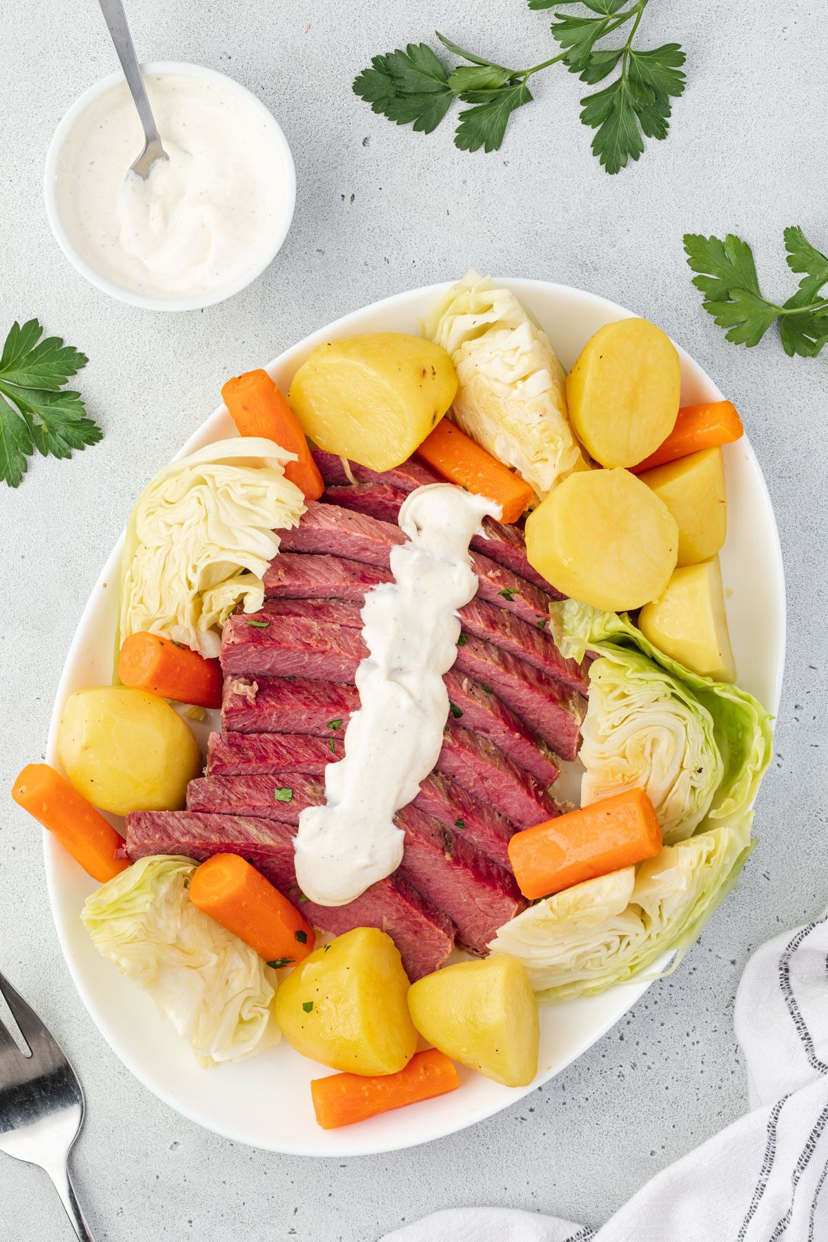 Overhead of corned beef and vegetables on a platter with tangy mustard sauce drizzled onto it and a bowl of mustard sauce in corner.