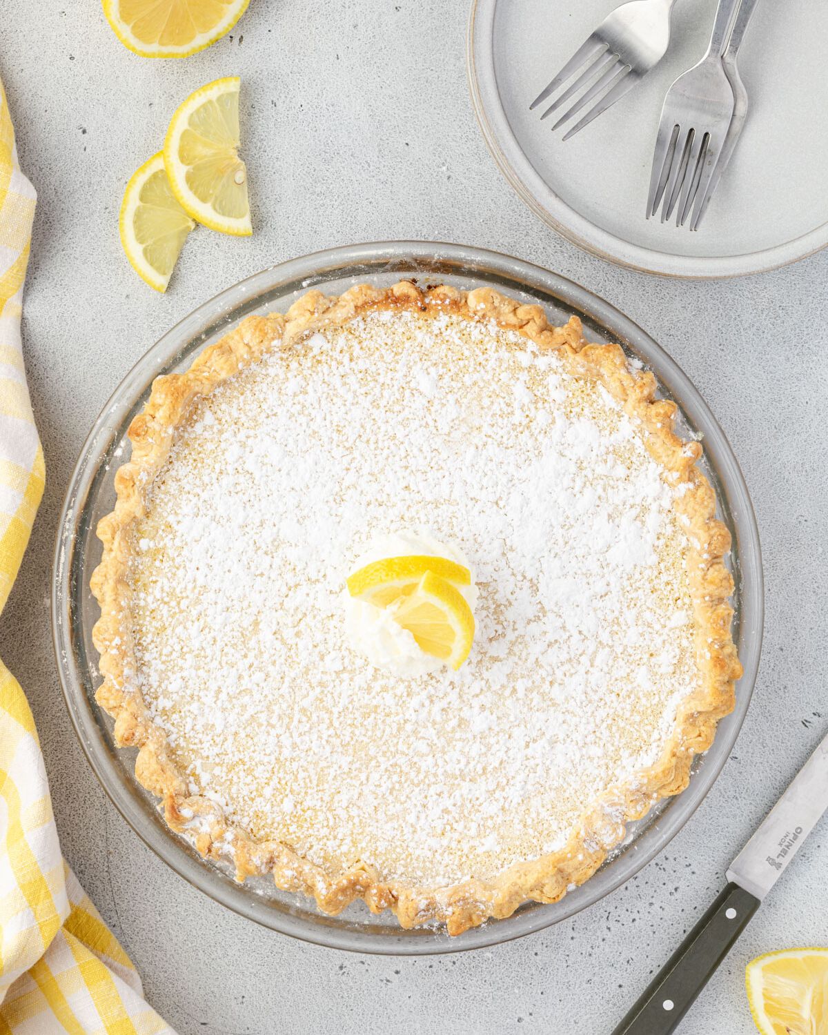 Overhead of the whole arizona sunshine pie, dusted with powdered sugar and toped with a dollop of whipped cream and a lemon slice.