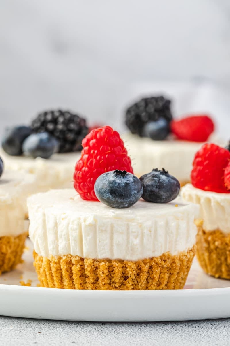 Individually portioned cheesecakes topped with berries on a platter, with one centered and close up.