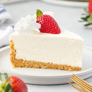 Slice of no-bake vanilla cheesecake on a plate with whipped cream and a half of a strawberry on top.