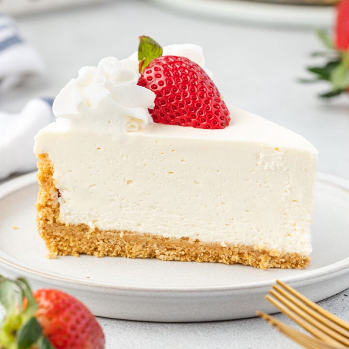 Slice of no-bake vanilla cheesecake on a plate with whipped cream and a half of a strawberry on top.