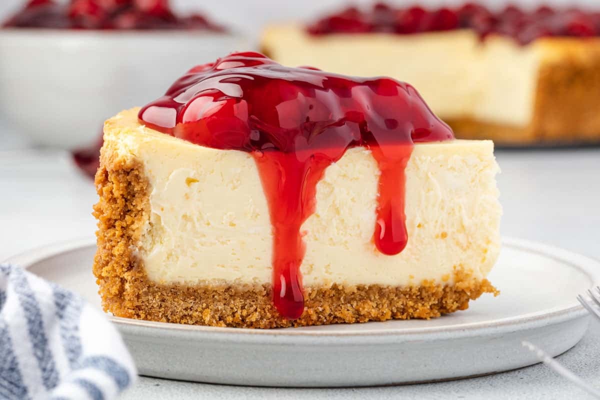 Side view of cheesecake on a plate with pie filling dripping down.