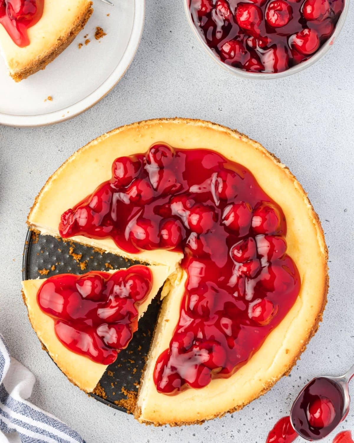 Overhead of philadelphia cheesecake, topping with cherry pie filling, and a slice is missing.