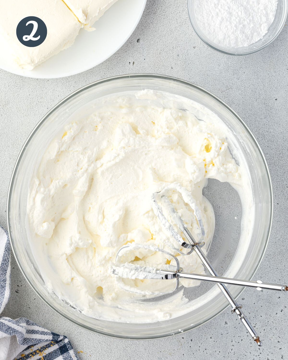 A bowl of whipped cream with two beaters resting crisscross inside the bowl.