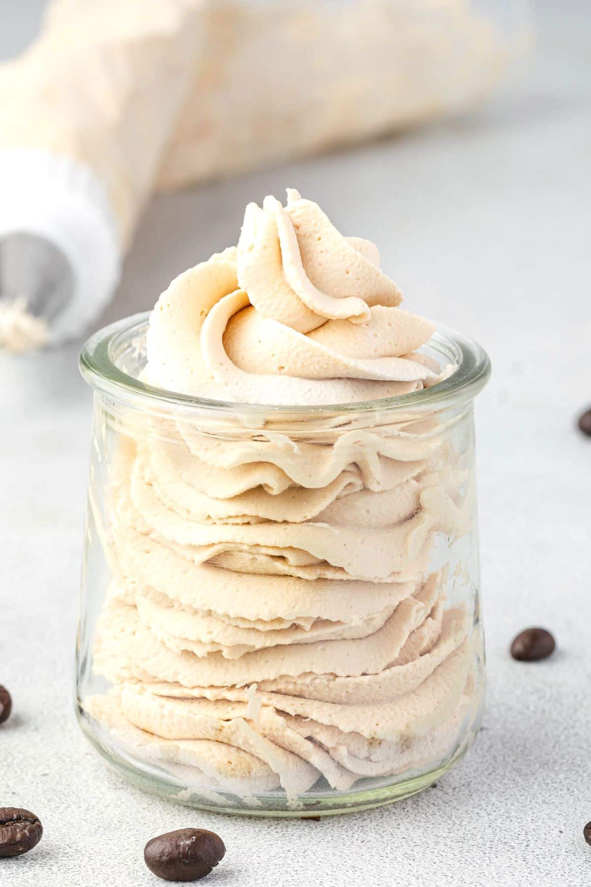 Coffee chantilly cream piped into a glass jar with a piping bag in the background.