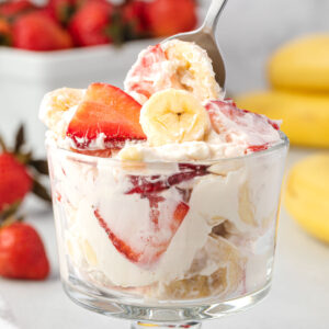 An individual parfait dish with strawberry banana cheesecake salad with a spoon dipping in.