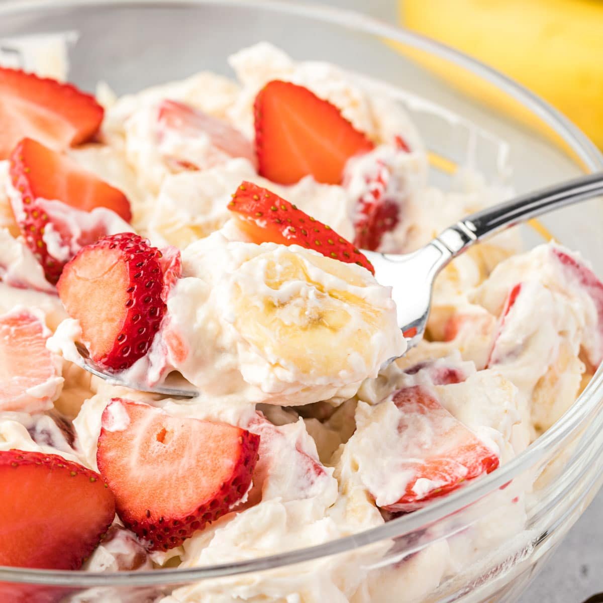 An individual parfait dish with strawberry cheesecake salad with a spoon dipping in.