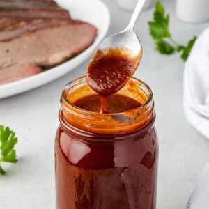 Side view of jar with tx bbq sauce dripping off spoon and brisket in background.