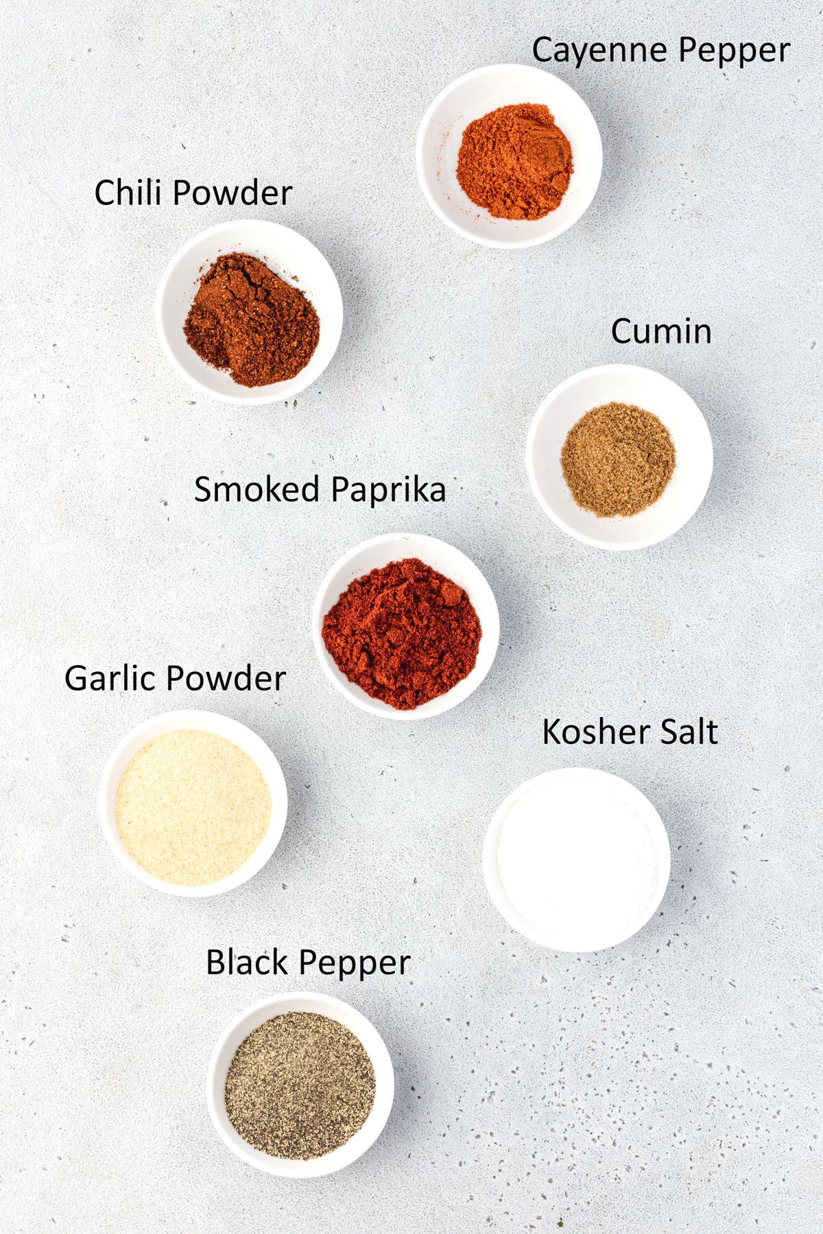 Overhead of the 7 ingredients used in this rub recipe, each in white pinch bowls.