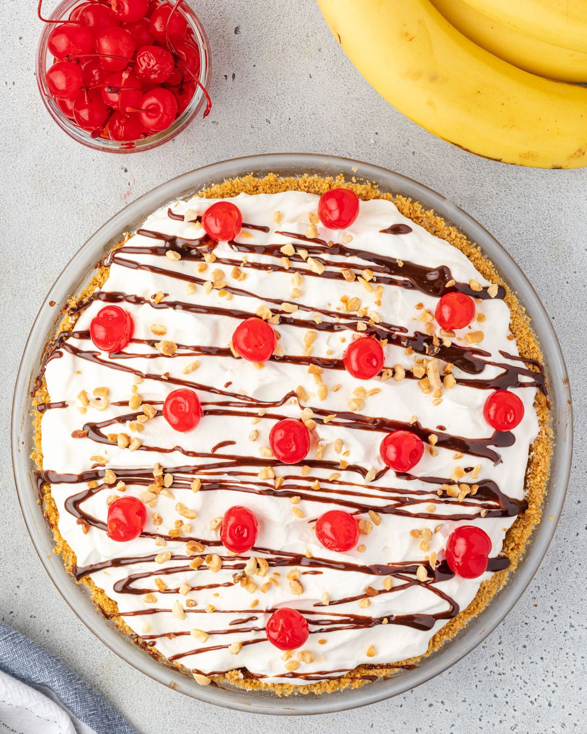 Overhead of the finished banana split pie with a jar of cherries and some bananas at top of image.