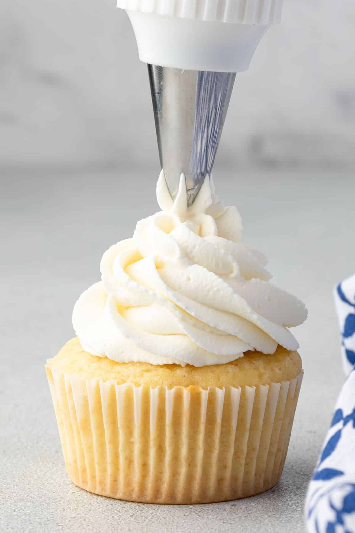 Piping stabilized whipped cream frosting onto a vanilla cupcake.