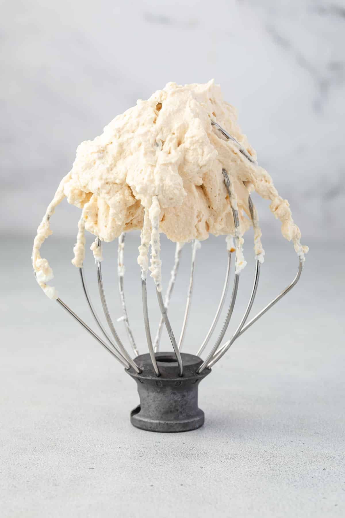 Caramel whipped cream on a whisk attachment standing up on the counter.
