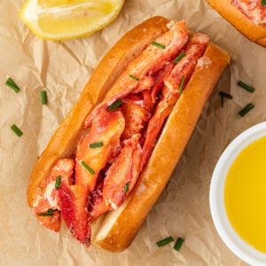 Buttery connecticut-style lobster roll on brown parchment with melted butter and lemon wedges.