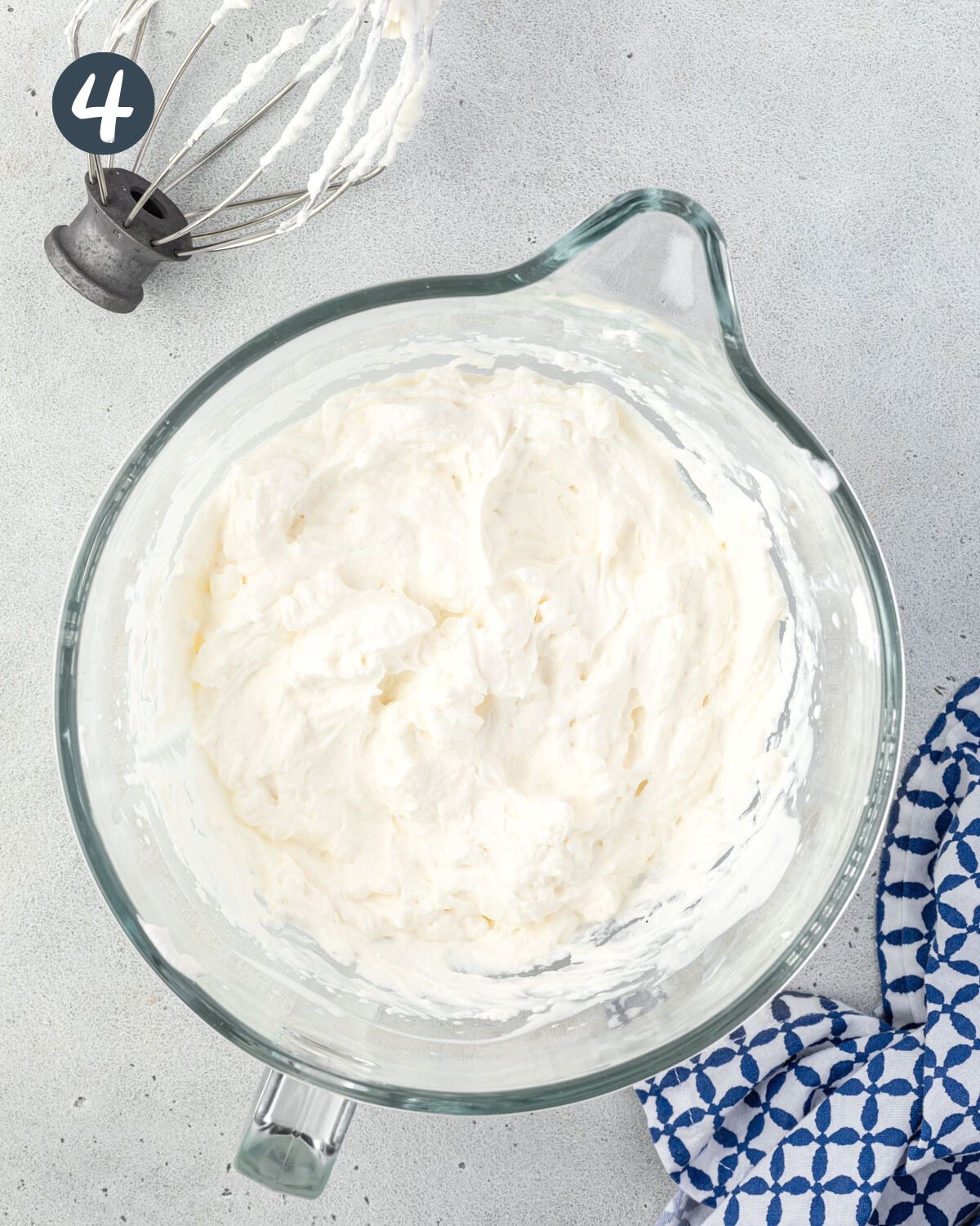 Large mixing bowl with fluffy whipped cream and whisk attachment above it.