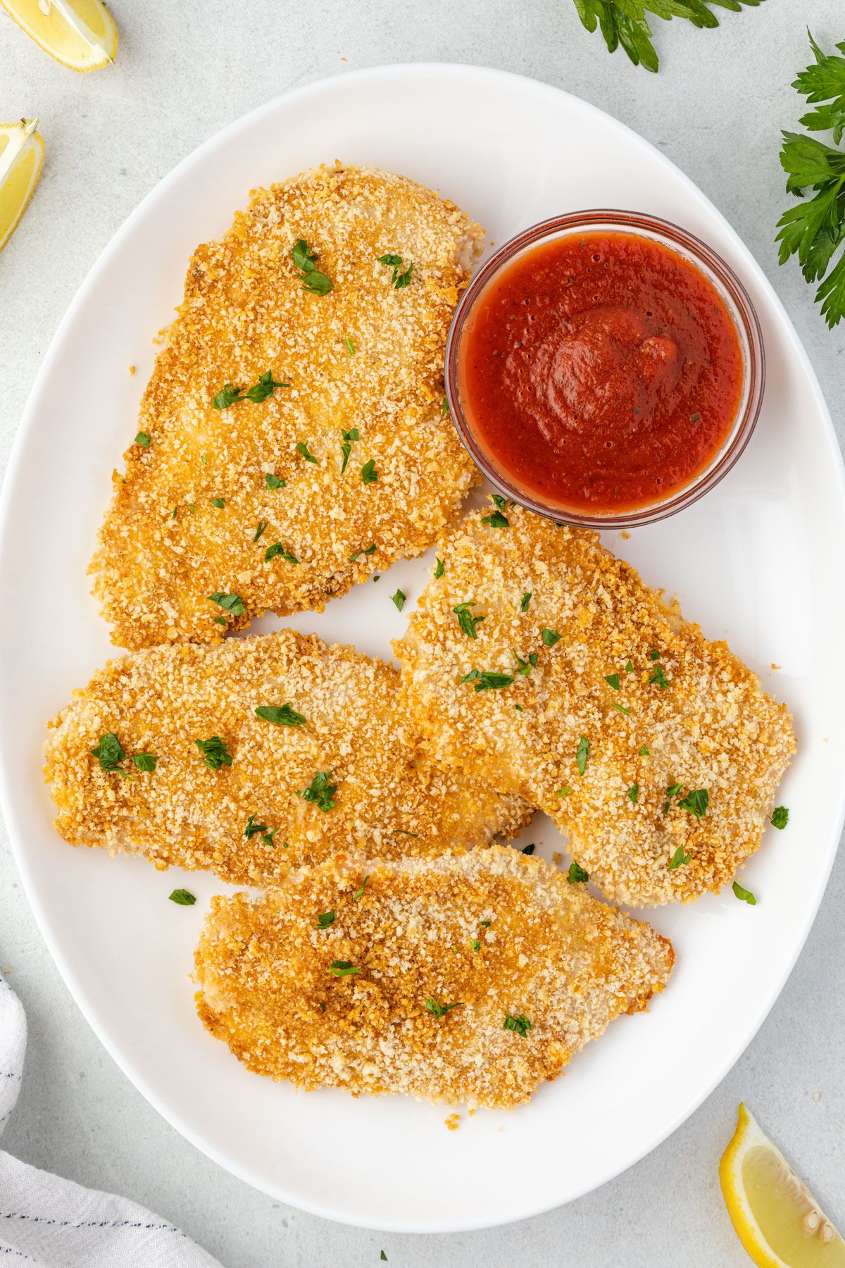 Overhead of 4 pieces of panko breaded chicken on an oval platter with a small bowl of marinara.