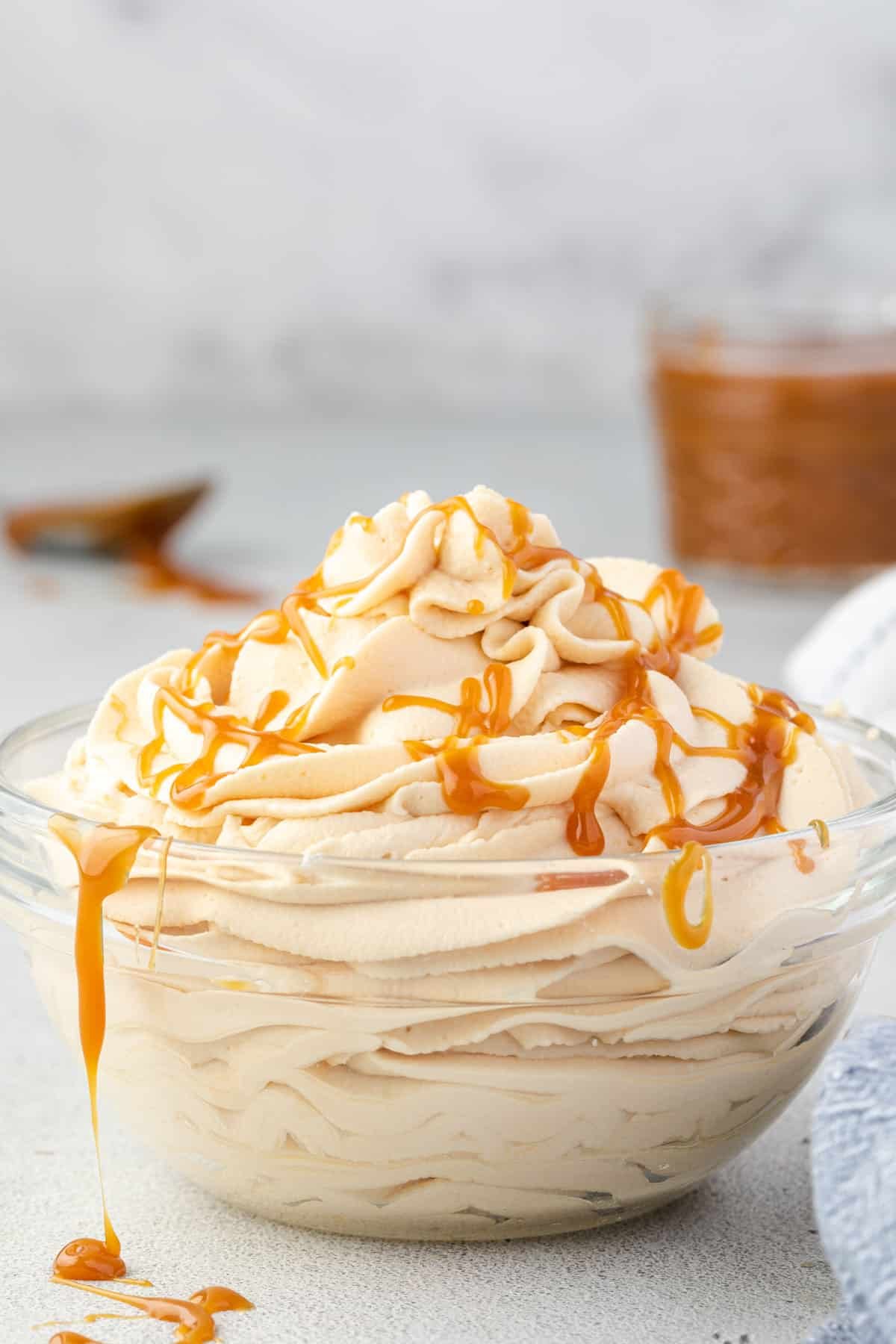 Whipped cream piled high in a bowl with caramel drizzled over it and dripping off of it.