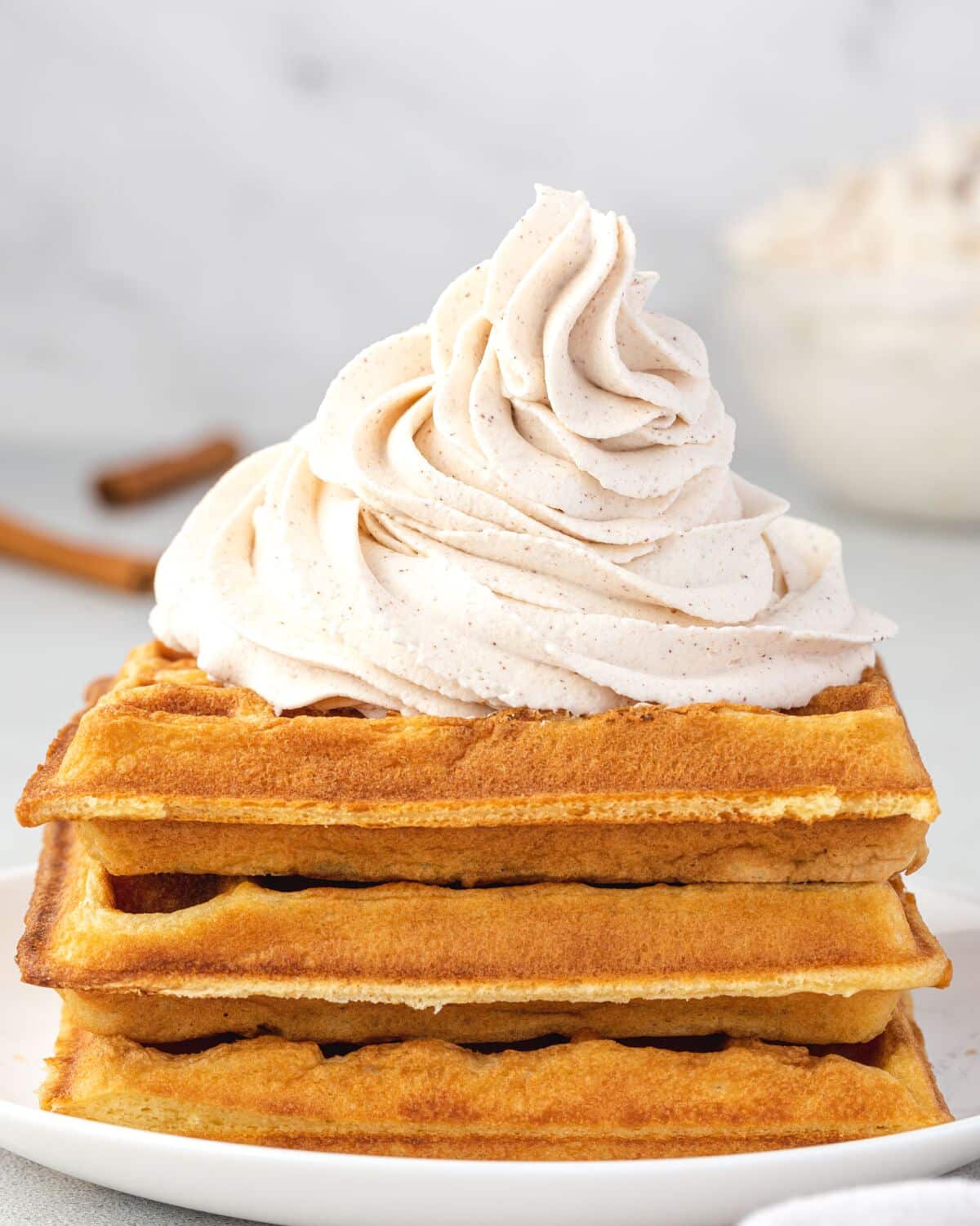 A stack of 3 waffles topped with a pile of piped whipped cream.