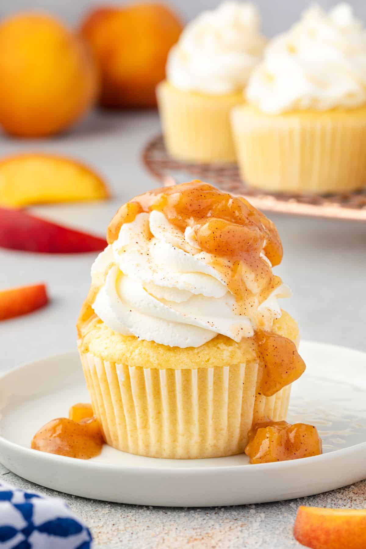Cupcake on a plate with whipped cream topping and peach filling dripping over the top of it.
