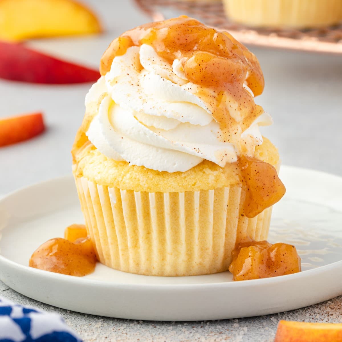 Side view of peach cobbler cupcakes on a platter, topped with whipped cream and fresh peach slices.