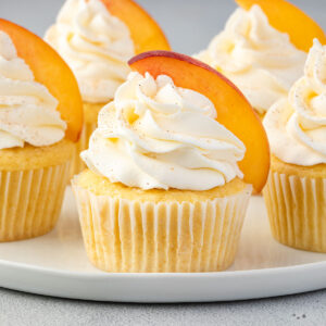 Side view of peach cupcakes on a platter, topped with whipped cream and fresh peach slices.