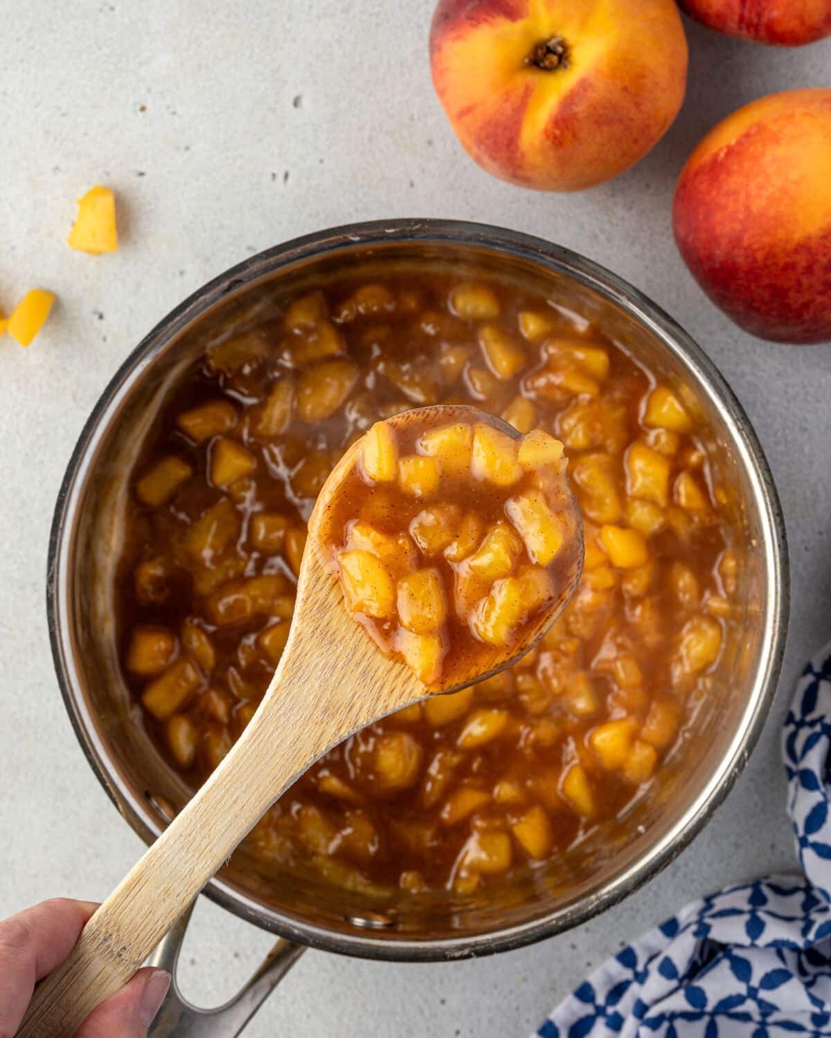 A wooden spoon with peach cobbler filling held over a saucepan.