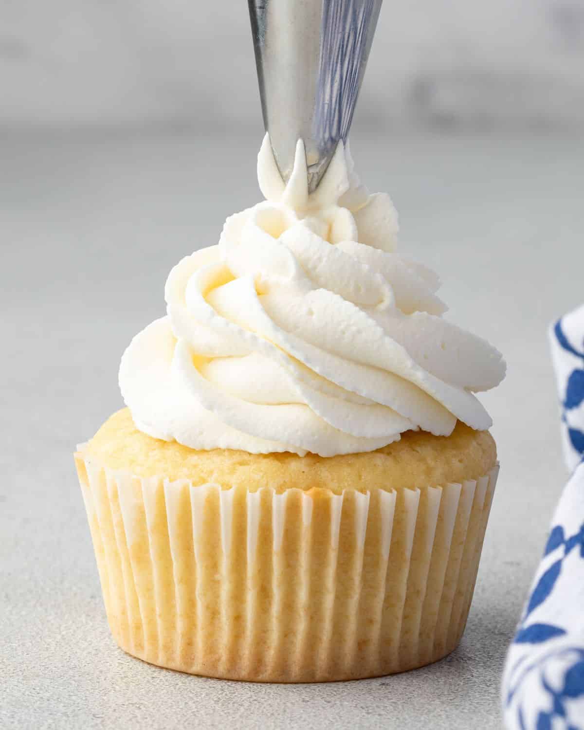 Piping whipped cream frosting onto cupcake.