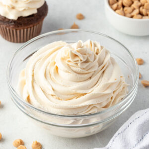 Peanut butter whippped cream piped into a bowl, frosted cupcake in one corner and bowl of peanut butter chips in another corner.