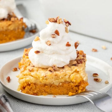 Square of sweet potato dump cake on a plate topped with whipped cream and nuts and a fork resting on the plate.