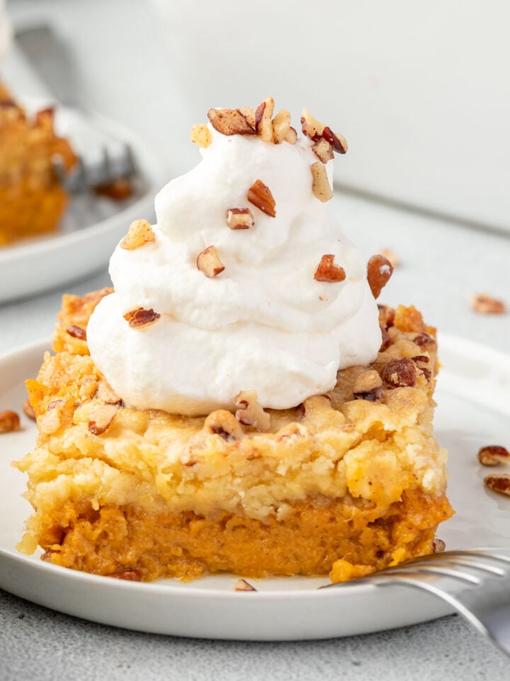 Square of sweet potato dump cake on a plate topped with whipped cream and nuts and a fork resting on the plate.