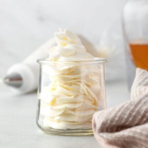 Jar of whipped cream with a piping bag and a jar of bourbon in background.
