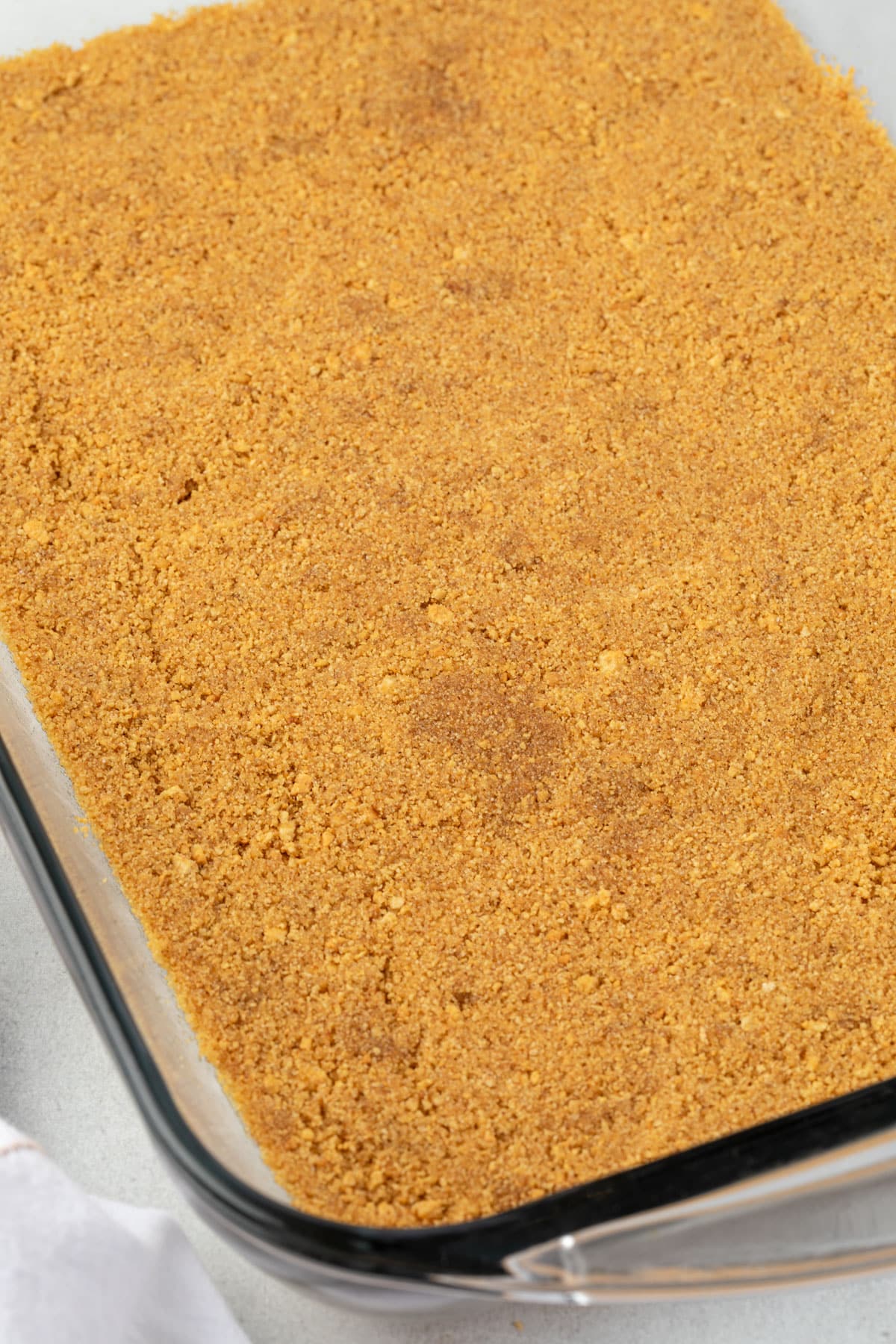 Golden graham cracker crust in a clear glass pan.