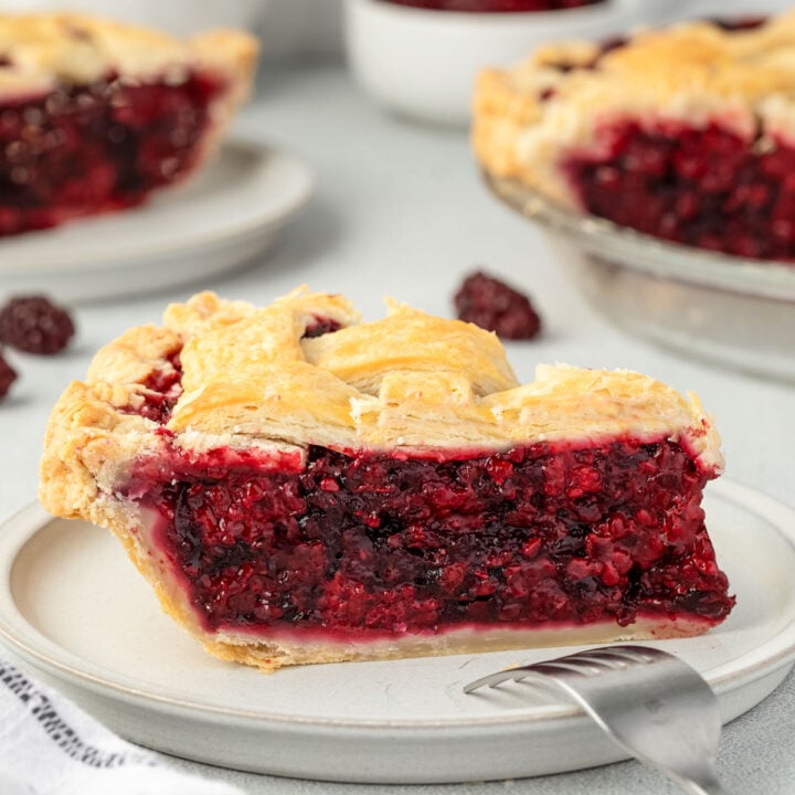 Vibrant red Marionberry pie topped with a lattice crust on a plate, with a fork turned over and resting on the plate.