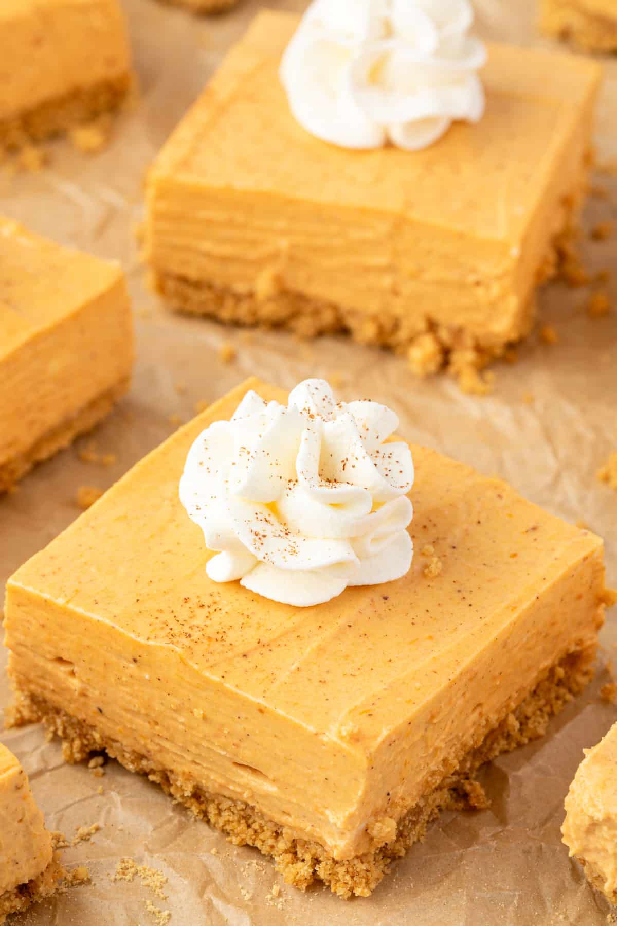 Square cheesecake bars on brown crumbled parchment, each square ha a dollop of whipped cream piped in the center.