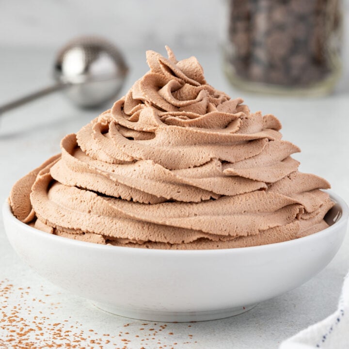 A white bowl with chocolate whipped cream piped in a swirl and cocoa powder dusting on counter.