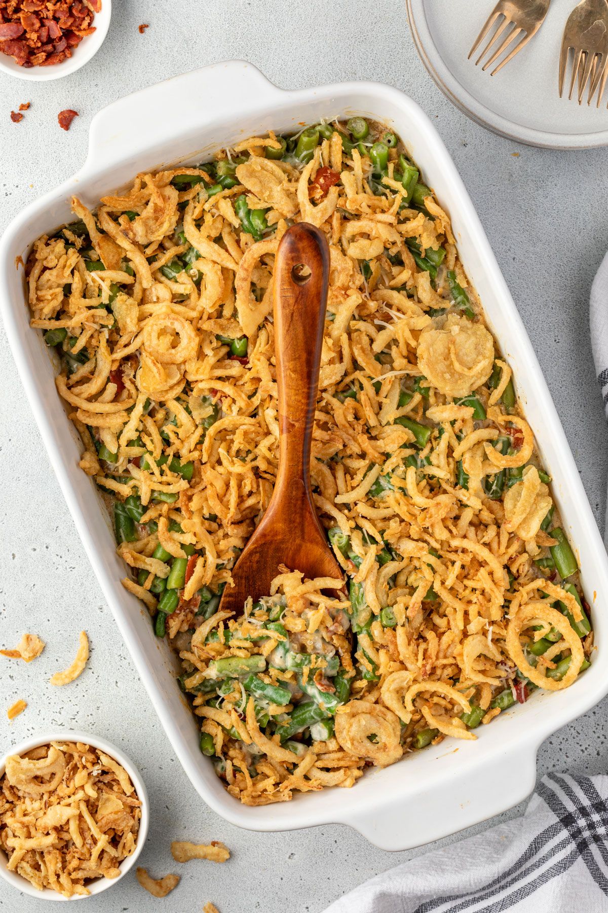 A 9x13 pan of green bean casserole with a wooden spoon scooping out a portion.