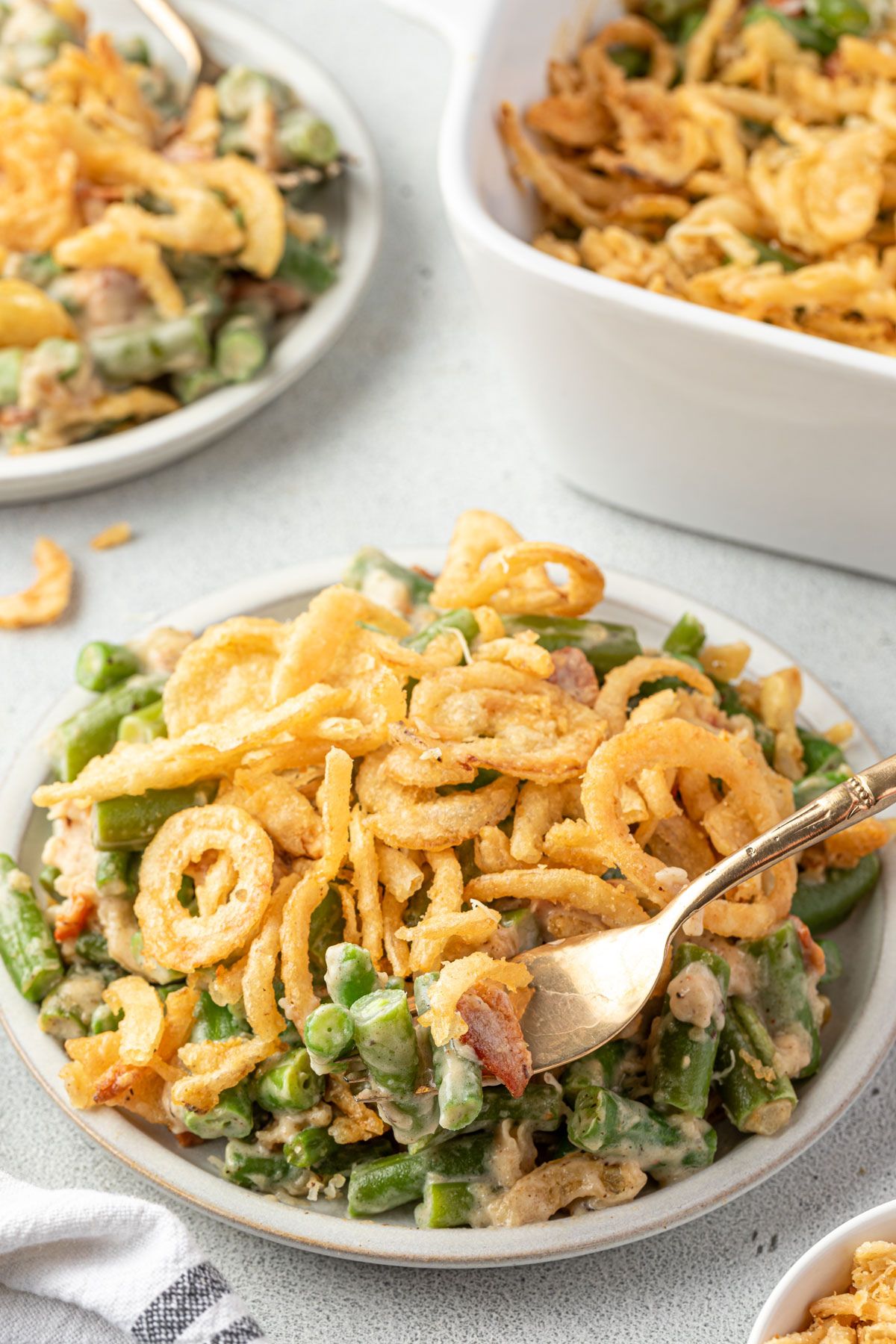 Green bean casserole topped with fried onions on a plate with fork scooping a bite.