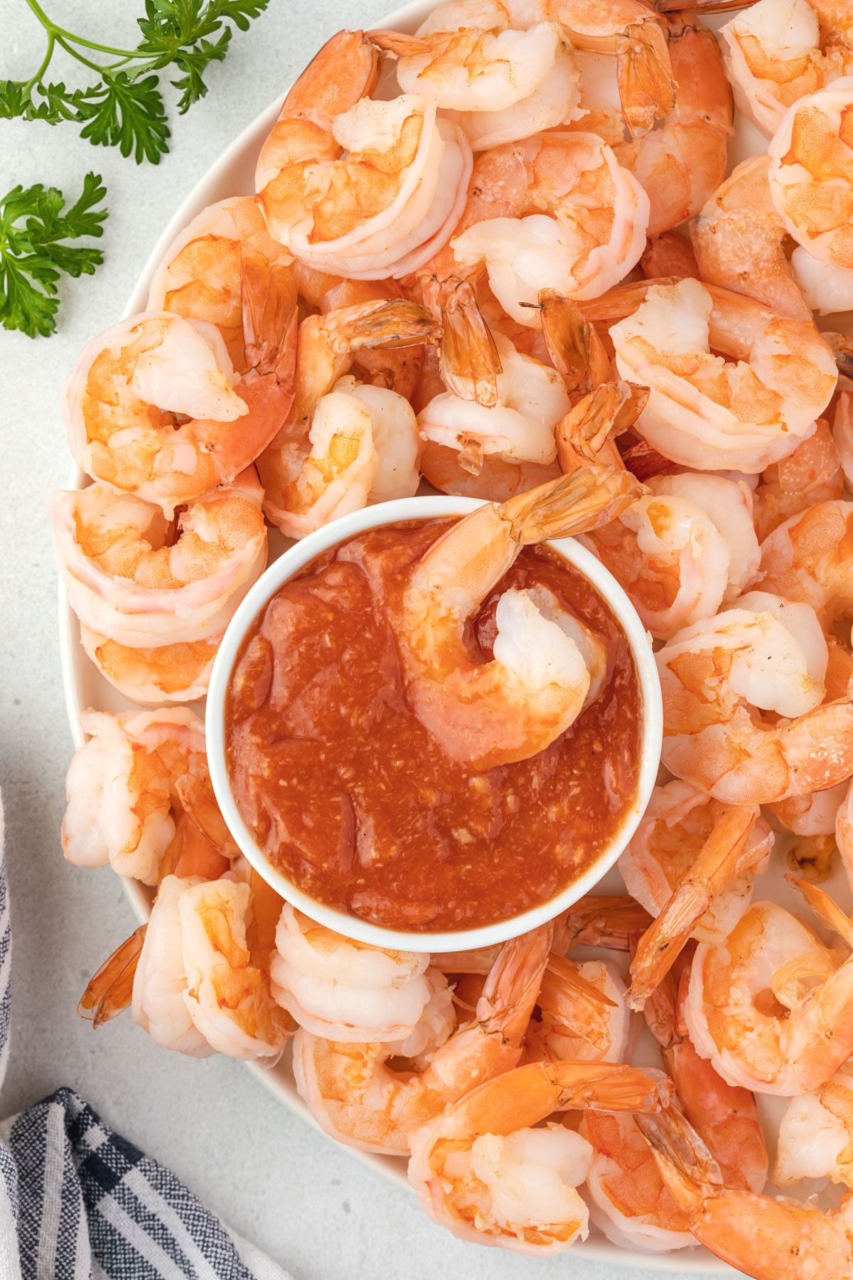 A white bowl filled with cocktail sauce with a shrimp on top sitting in the center of a platter of shrimp.