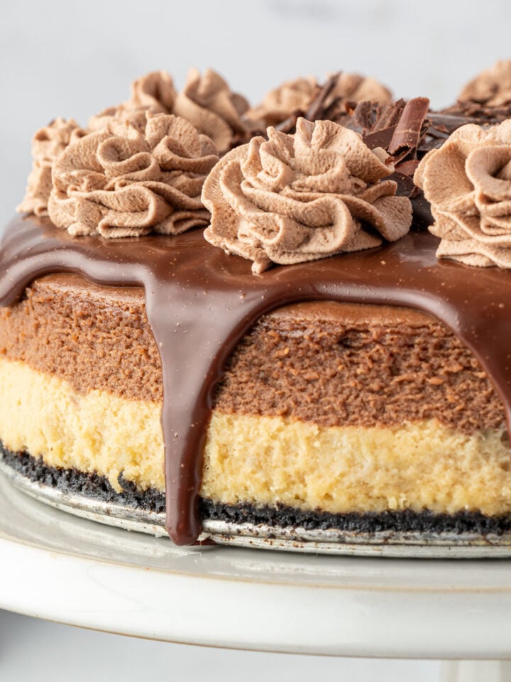 Layered mocha cheesecake with chocolate ganache drips and chocolate whipped cream.