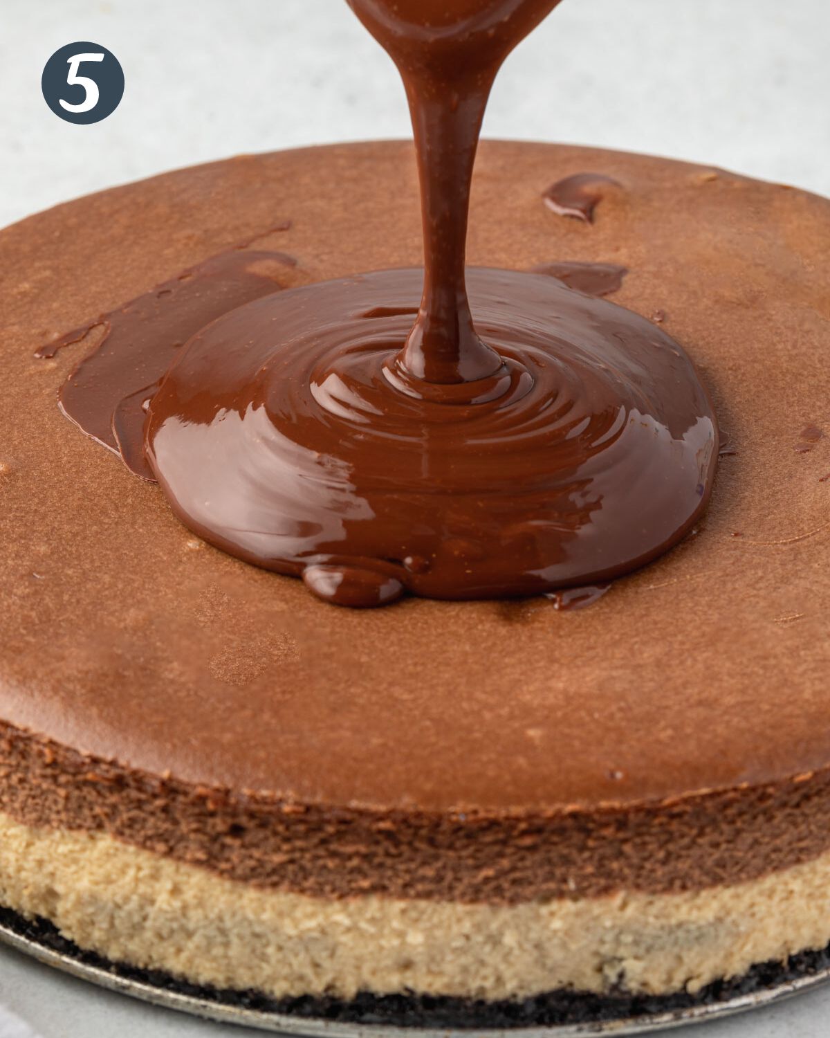 Chocolate ganache poured on top of the cheesecake, with a ring of ganache pooling in the center.