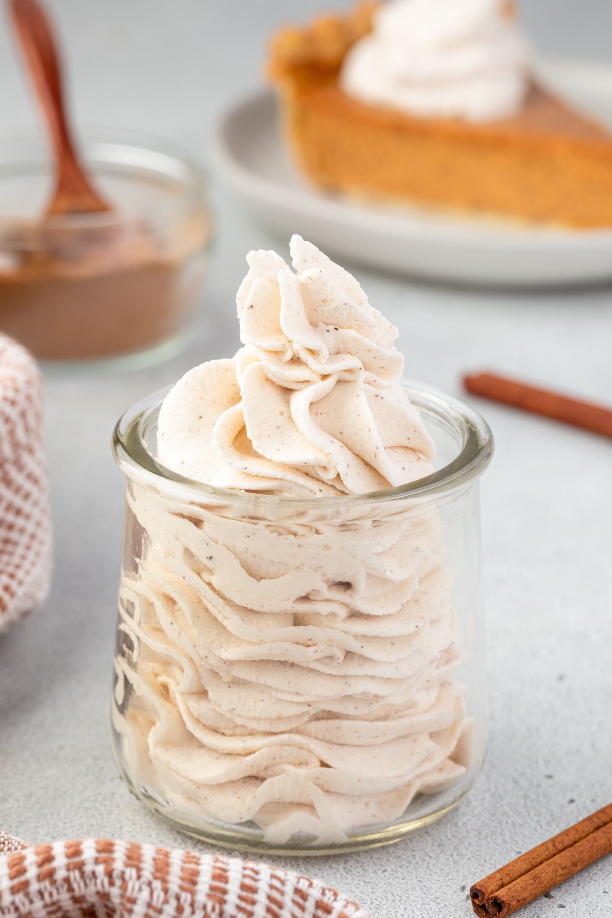 Spiced whipped cream piped in a glass jar with cinnamon sticks surrounding.