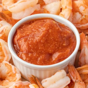 A white bowl filled with red sauce surrounded by shrimp cocktail.