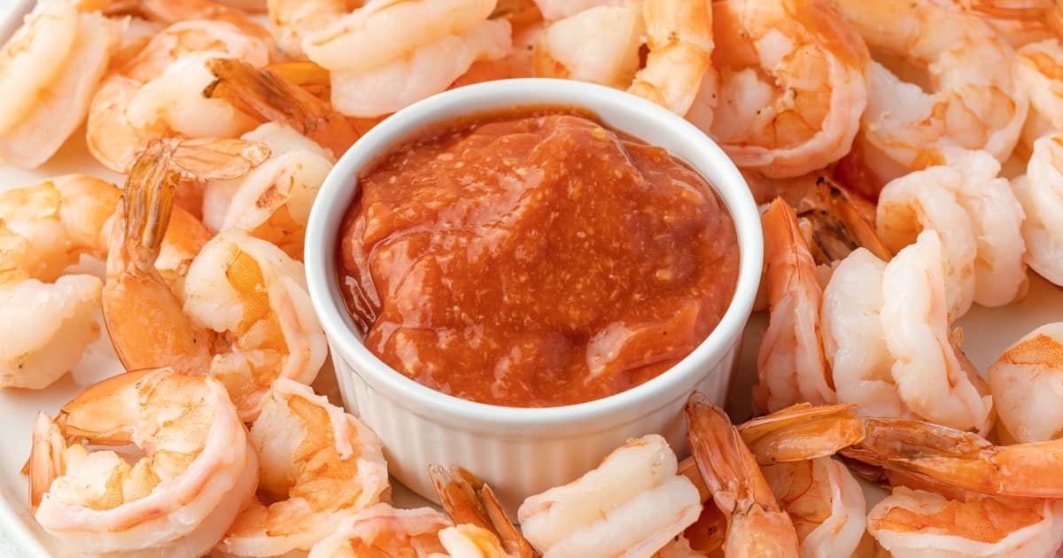 A platter of jumbo shrimp cocktail with a bowl of cocktail sauce in the center.
