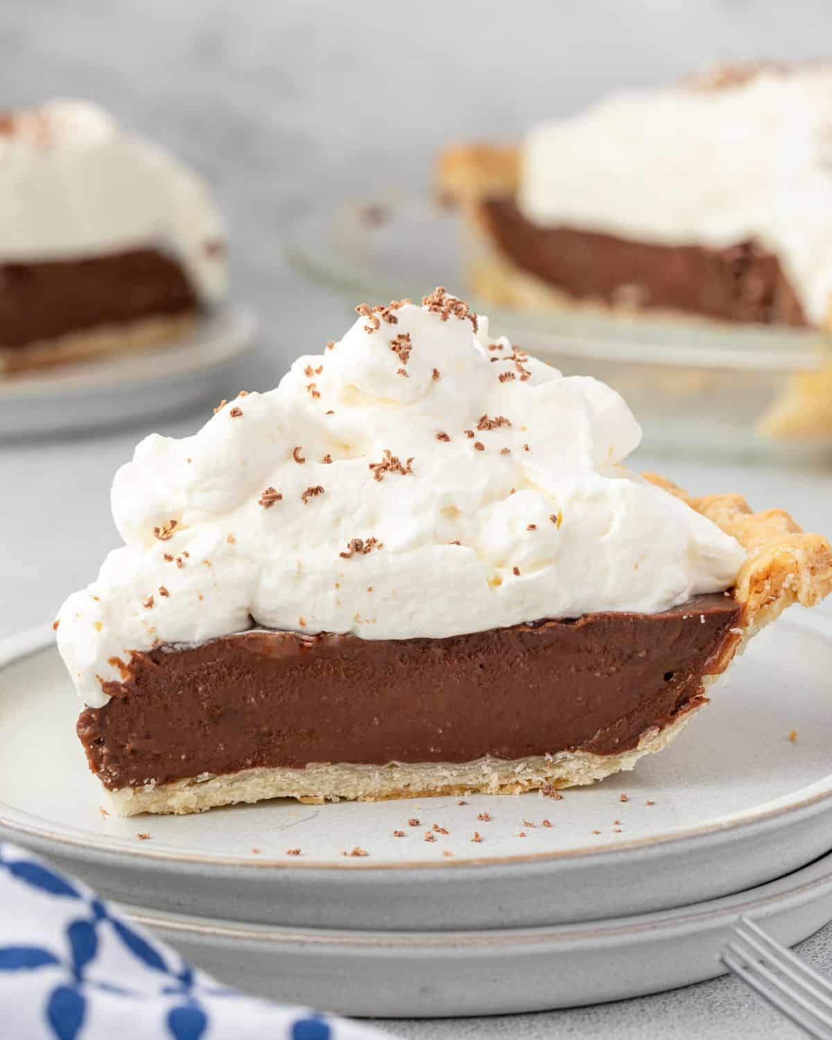 Slice af chocolate pie topped with whipped cream on a stack of plates.