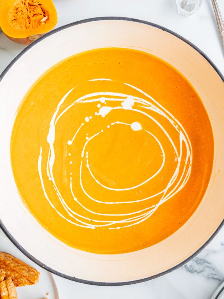 Butternut squash red pepper soup in a large pan with swirls of cream.