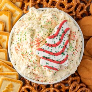 Cream cheese dip with red and green sanded sugar sprinkles in a white bowl, garnished with a Christmas tree cake.