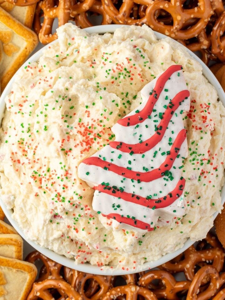 Cream cheese dip with red and green sanded sugar sprinkles in a white bowl, garnished with a Christmas tree cake.